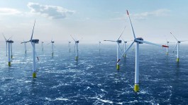 Blick auf einen Offshore-Windpark mit mehreren weißen Windturbinen auf gelb markierten Fundamenten im offenen Meer bei leicht bewölktem Himmel; die Wellenoberfläche schimmert im Sonnenlicht. 